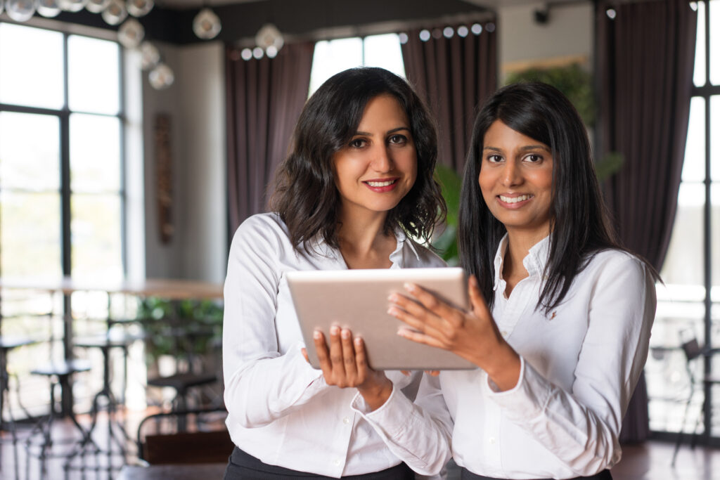 two smiling female coworkers using tablet computer in cafe